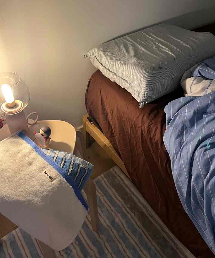 Bedroom with harmonious wood tone and blue hues, featuring wooden bed frame, striped rug, soft towels and warm table lamp creating cozy atmosphere