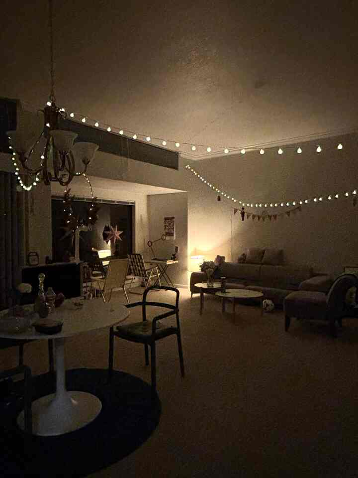 Warmly lit two-person living room featuring white round table and sofa with garland decorations creating cozy Christmas vibe