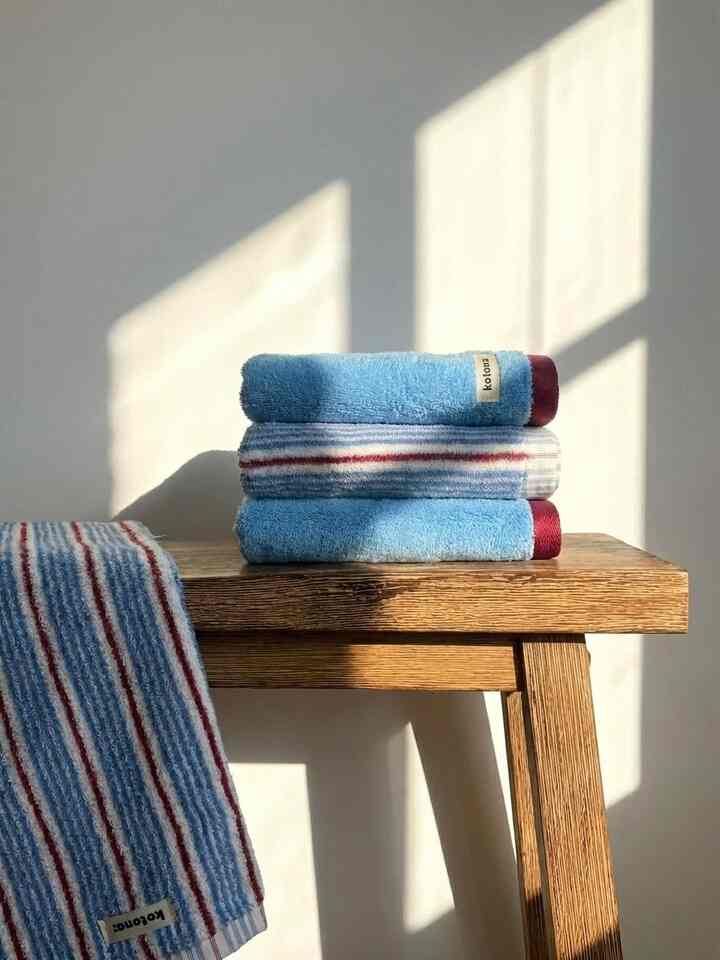 Soft blue-toned towels stacked on natural wood bench in a cozy corner brightened by sunlight