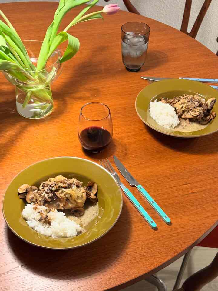 Warm brown tone dining table featuring dining chairs, olive green bowls, cutlery, and a vase creating a cozy dining atmosphere