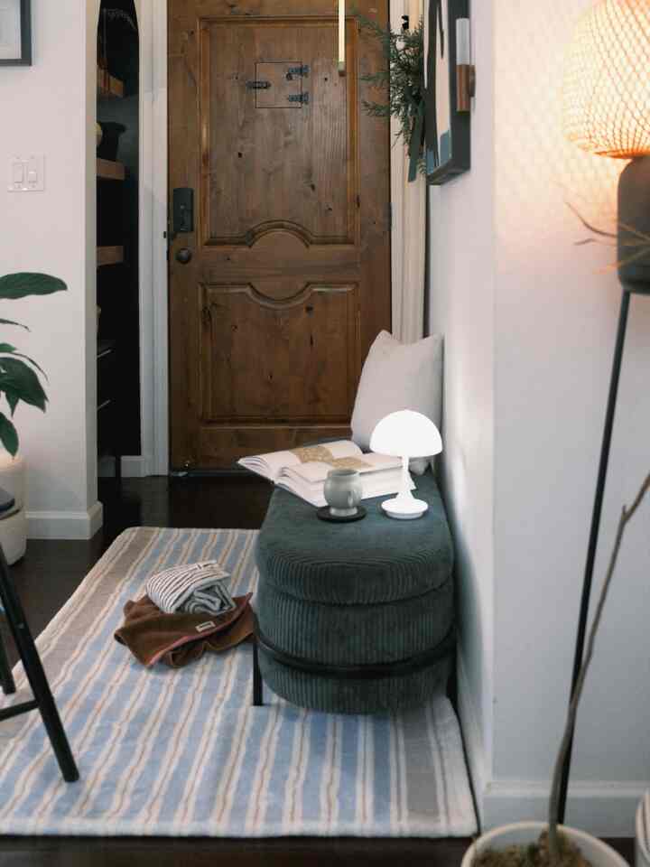Cozy entrance featuring blue striped rug, wood tone door, ottoman with small mood lamp creating warm atmosphere