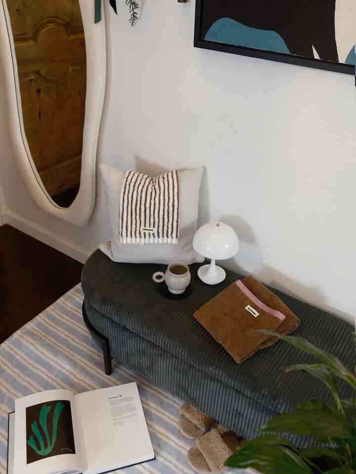 Calm green-toned ottoman with striped rug, mirror, and cushion arranged in an entrance space