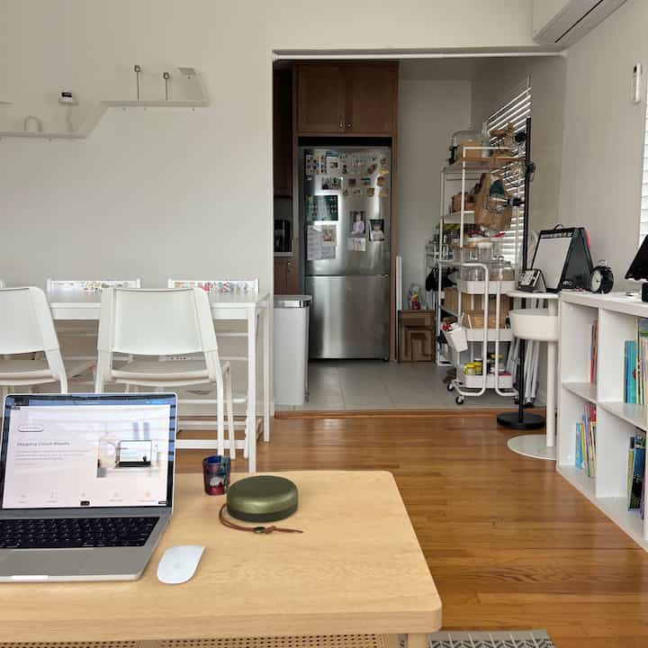 White and wood tone living room and kitchen space featuring laptop and bookshelf with cozy home office setup