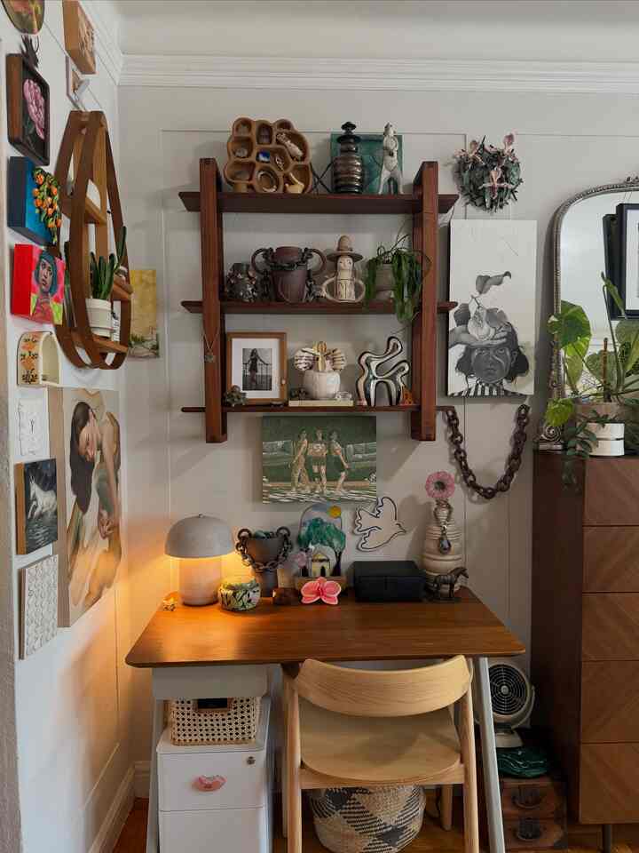Warm wood tone mid-century modern bohemian home office featuring eclectic art collection and a glowing table lamp