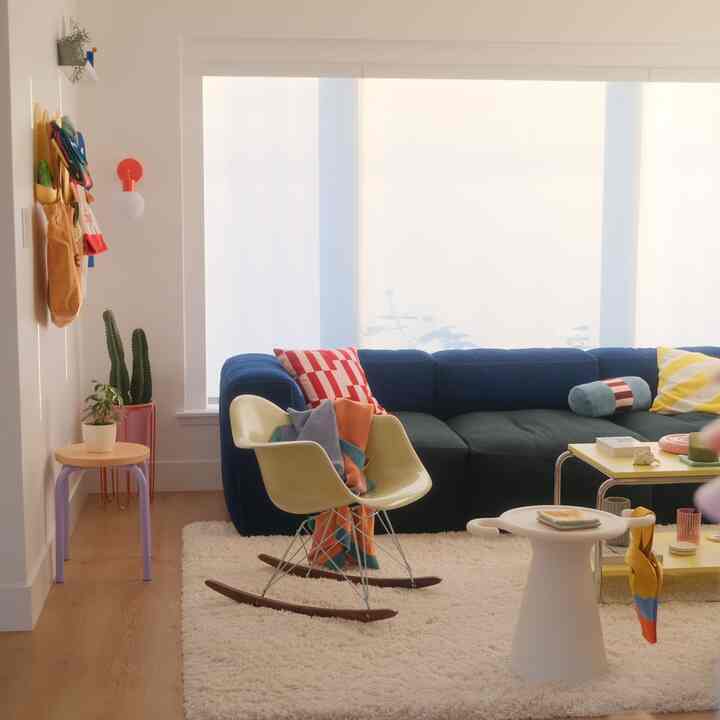 Bright cozy living room featuring a blue sectional sofa, yellow cushions, and natural wood flooring under soft golden hour light