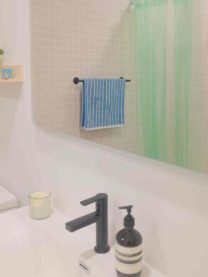 White and green toned bathroom featuring a white sink with matte black faucet, blue striped towel on rack, and green shower curtain creating a fresh atmosphere