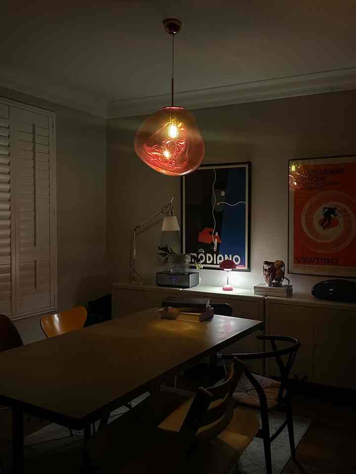 Warm pink lighting accentuates modern dining room with diverse chairs, creating a cozy nighttime atmosphere