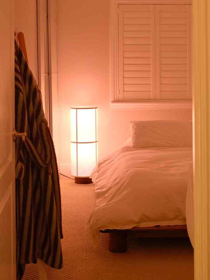 Cozy white bedroom illuminated by warm floor lamp featuring wood bed frame and soft bedding