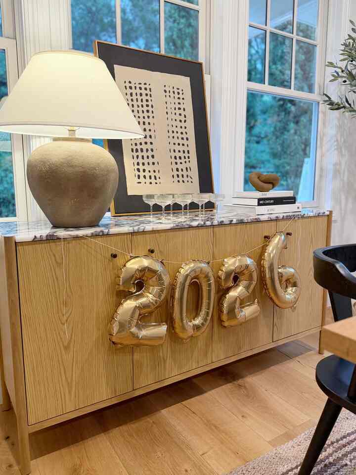 Bright living room featuring a wood tone sideboard decorated with a table lamp and gold balloons