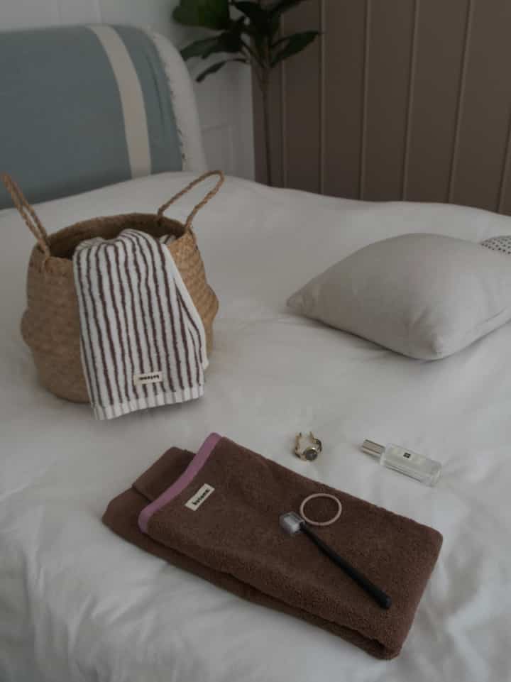 Beige and brown toned bedroom featuring a woven basket, Kotona towels neatly placed on bed, creating a cozy and natural atmosphere