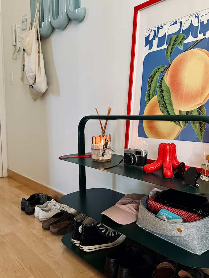 Clean entrance with white walls and dark green shoe cabinet, featuring a red-framed poster and decorative objects as accents