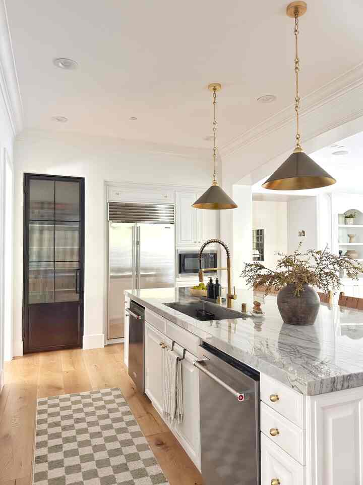 Modern kitchen with white walls and wood tones, featuring marble countertop and gold pendant lights for a sleek look