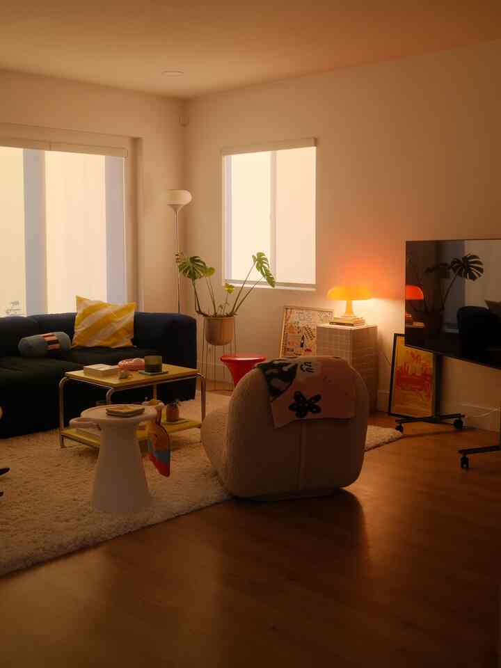 Cozy living room with warm natural colors, featuring a dark sofa, white stool, and orange table lamp creating a sunset ambiance