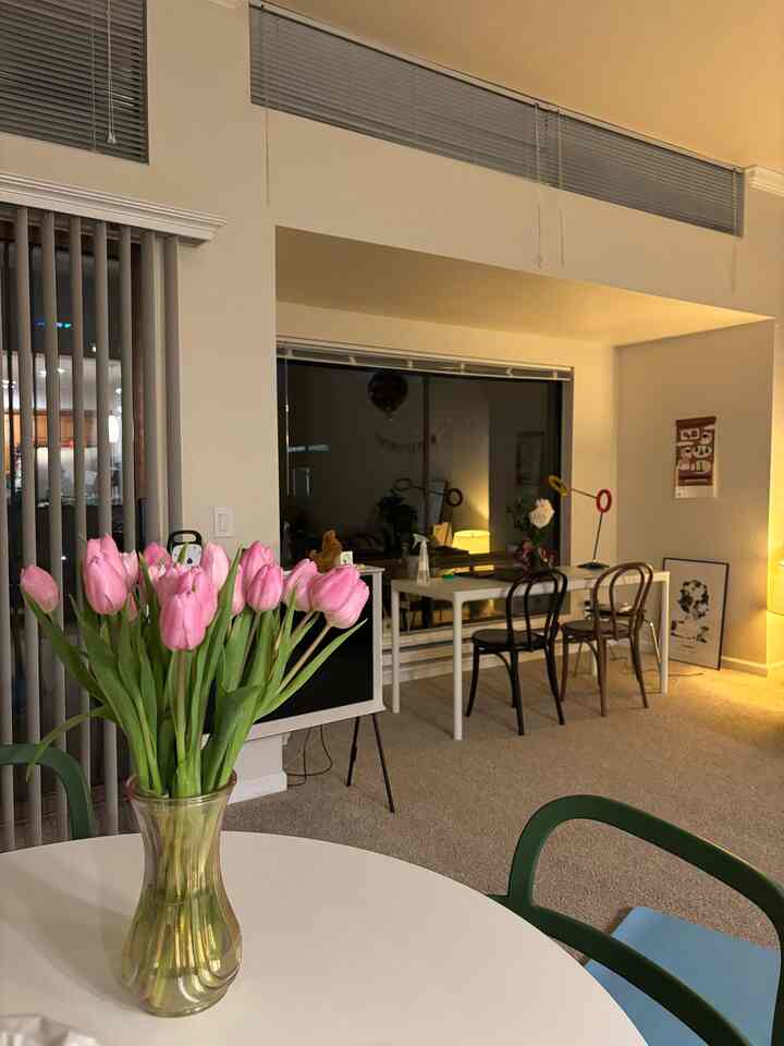 Natural-toned living room featuring a white table with a transparent vase of pink tulips, and a desk with chairs and lamps