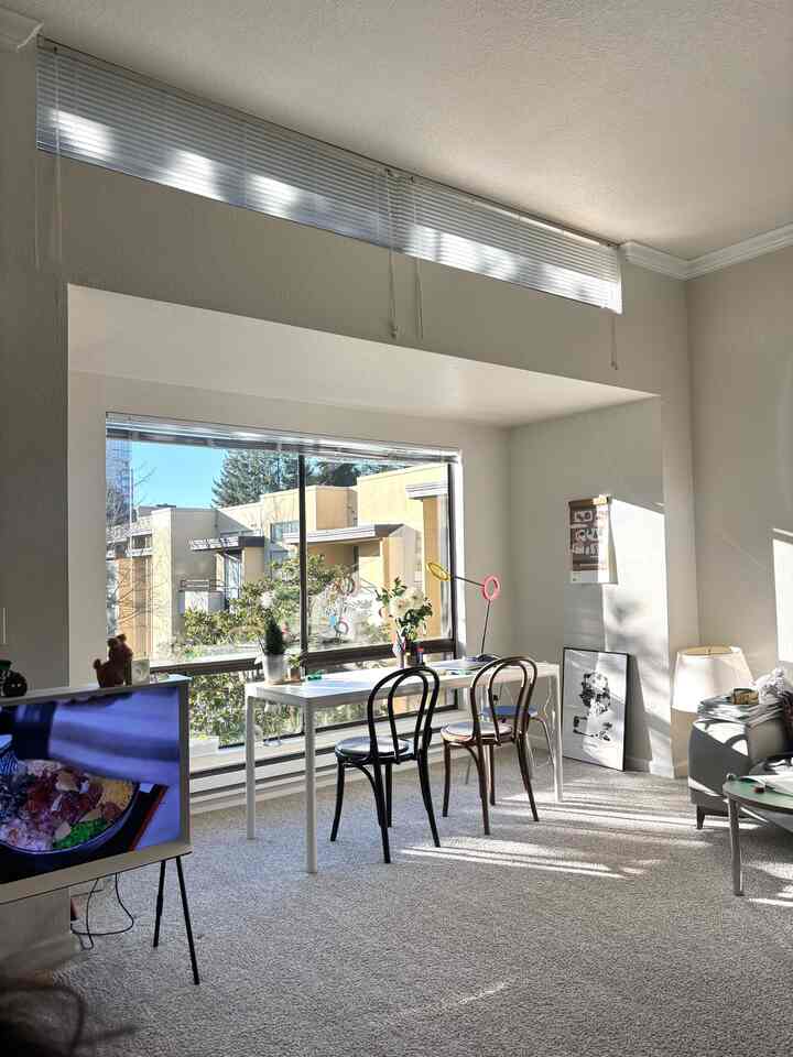 Bright white and gray toned living room and home office with a large window, featuring a clean modern desk setup with two chairs