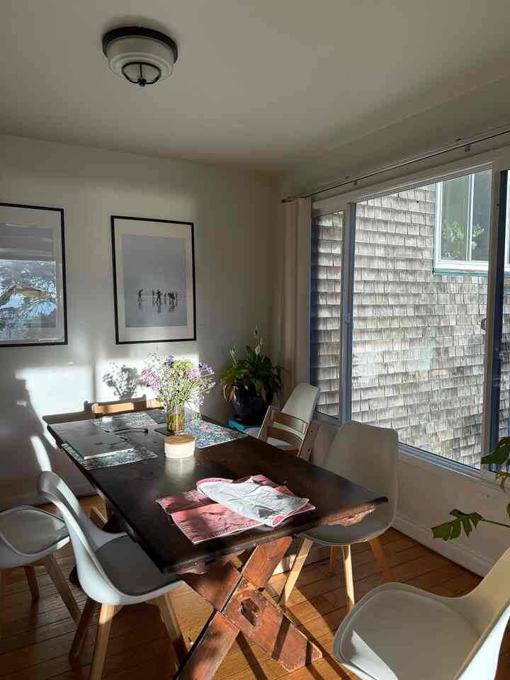 A white and wood tone dining room featuring a large dining table and chairs bathed in warm sunlight, evoking a family atmosphere