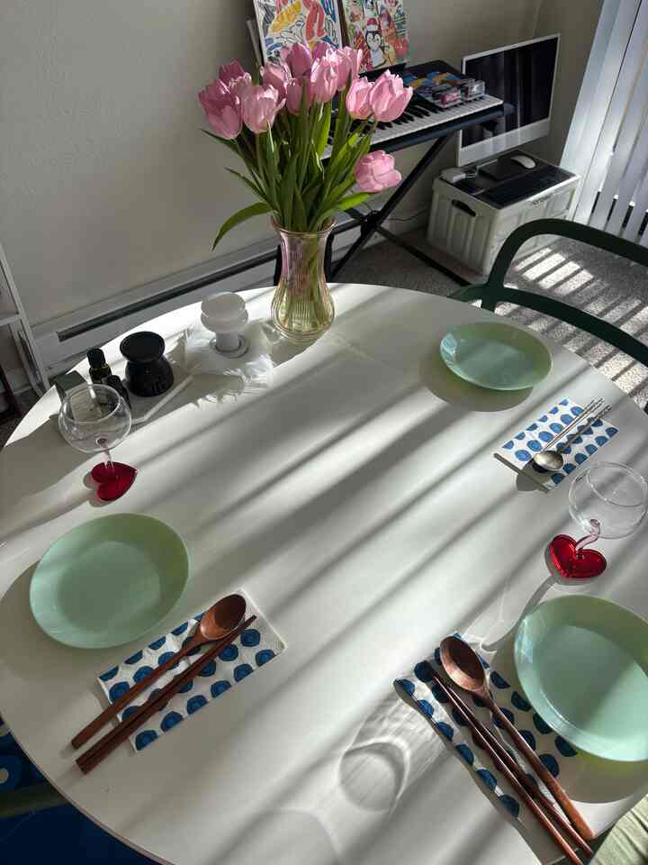 White-toned dining room featuring a round table with mint plates and a vase of pink tulips, creating a cozy home party atmosphere