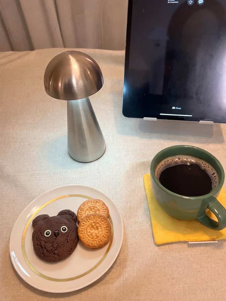 Beige-toned table with a chrome silver mushroom lamp, coffee mug, and cookies creating a simple home cafe setting