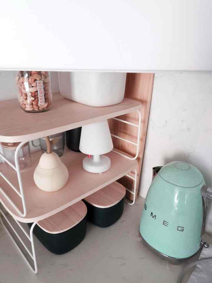 Natural tone kitchen corner featuring a SMEG electric kettle and a small table lamp on organized shelves, creating a clean cozy atmosphere