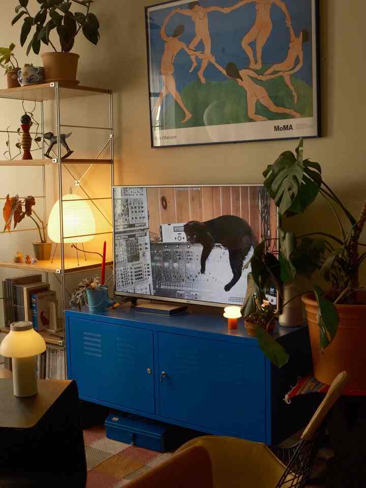 Cozy living room with warm beige walls and vivid blue TV console, featuring various table lamps and plants, creating an Instagrammable atmosphere