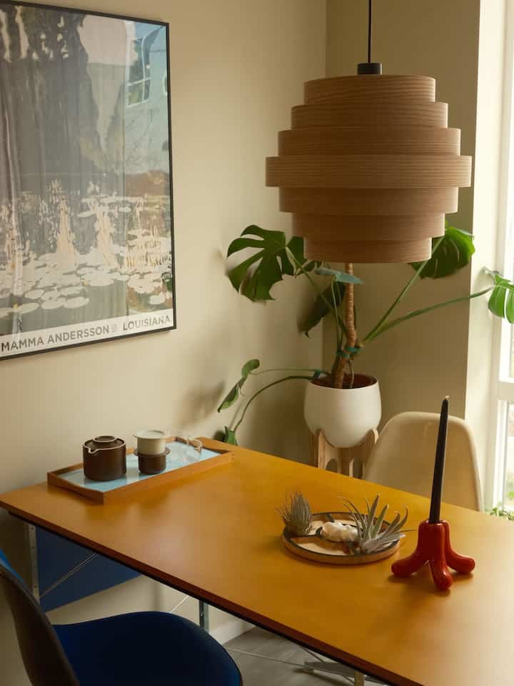 Beige and wood tone home office featuring an Eames desk, plants, and a wooden pendant light creating a cozy atmosphere