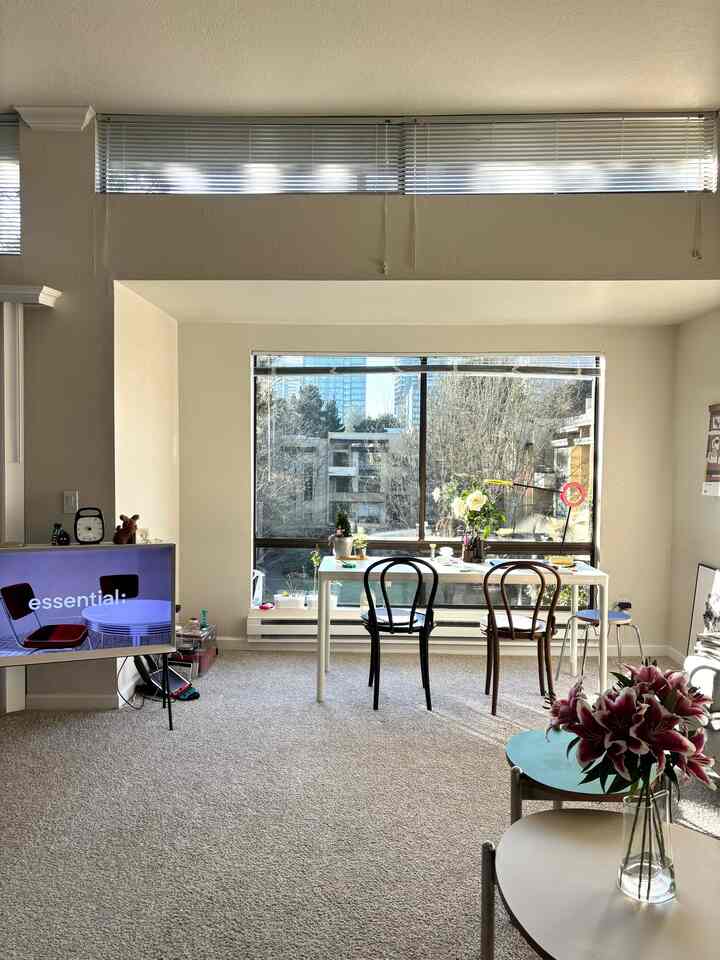 Bright white-toned living room featuring a desk with chairs by the window, a TV stand, and a flower vase creating a cozy atmosphere