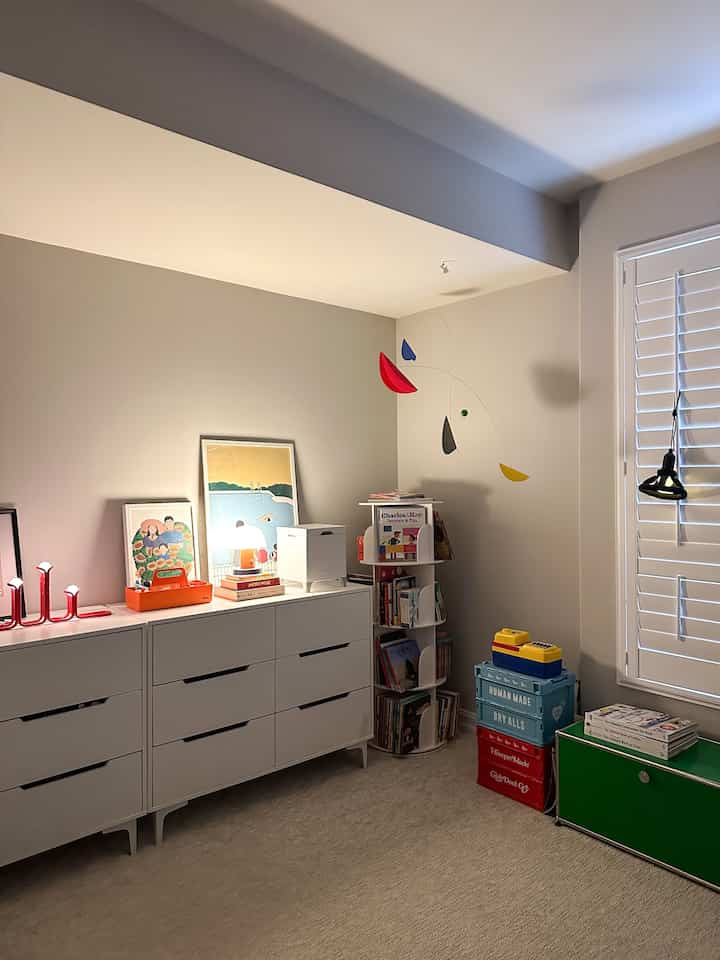 White-walled kids' room featuring storage cabinets, table lamps, and colorful storage boxes creating a cozy atmosphere