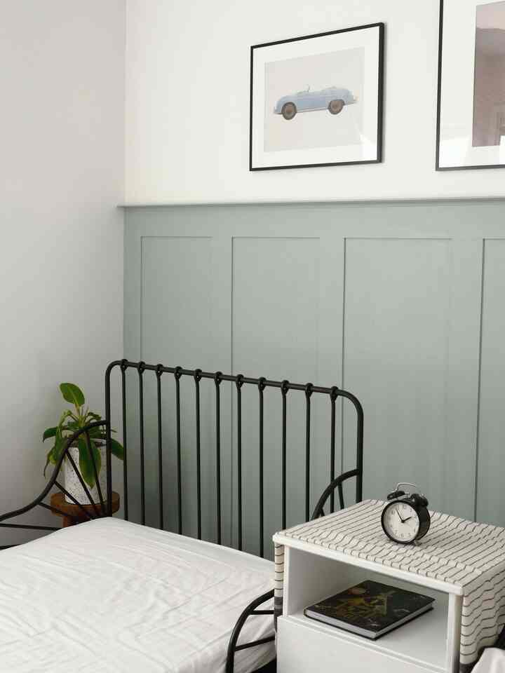 White and wood tone bedroom featuring a black metal bed, clock on a side table, and framed artwork with a clean design