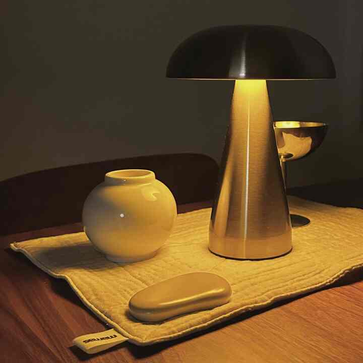 Warm wood tone dining room table featuring a chrome silver table lamp and white decorative objects, creating a moody atmosphere