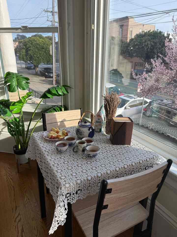 Bright white lace-covered dining table with tea set and green Monstera plant in a cozy cafe-style two-person space