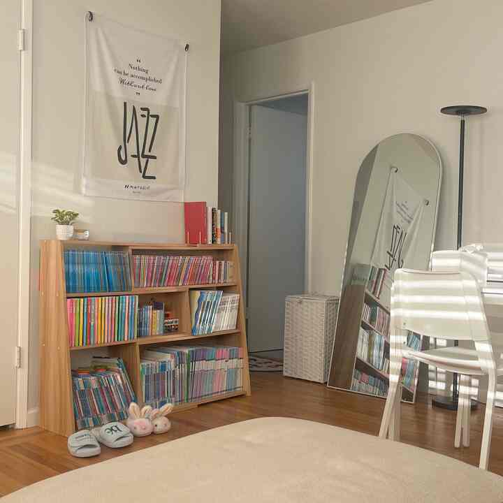 Natural-tone living room featuring wood bookshelf, large full-length mirror, and floor lamp in a cozy setting