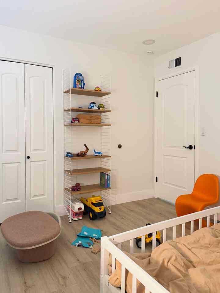 White and beige toned kids' room featuring an orange chair and storage shelves with a minimal and natural atmosphere