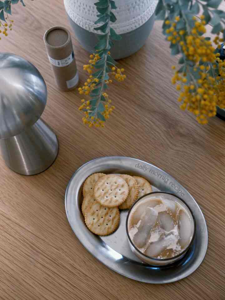 Light brown wooden tabletop featuring a small stainless steel plate and iced beverage in a minimalist Nordic style setting