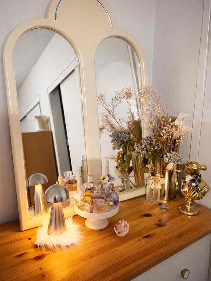 Wood tone table featuring a silver table lamp, gold vases, and decorative objet in a calm bedroom mirror setting