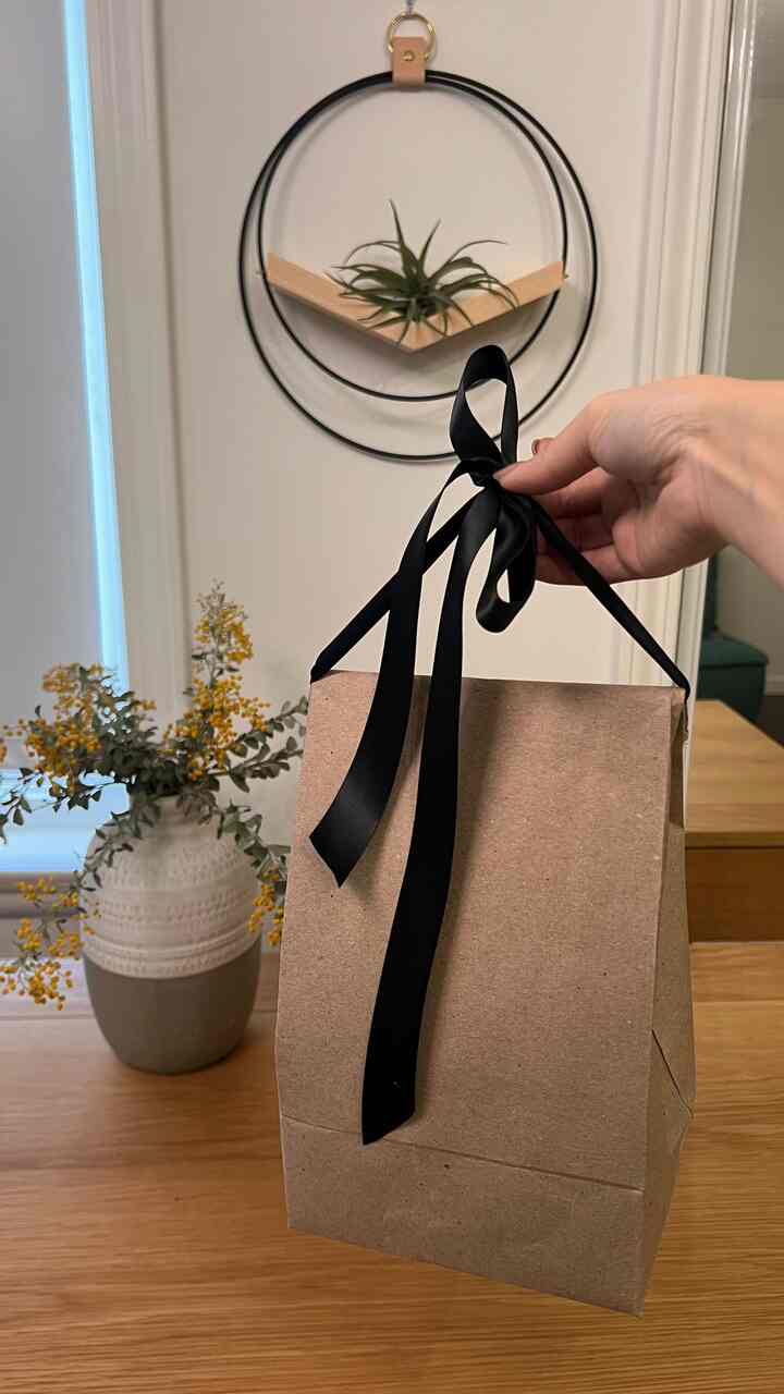 Natural-toned home office space featuring a wooden desk with shelf, vase, and a gift tied with a black ribbon creating a modern atmosphere