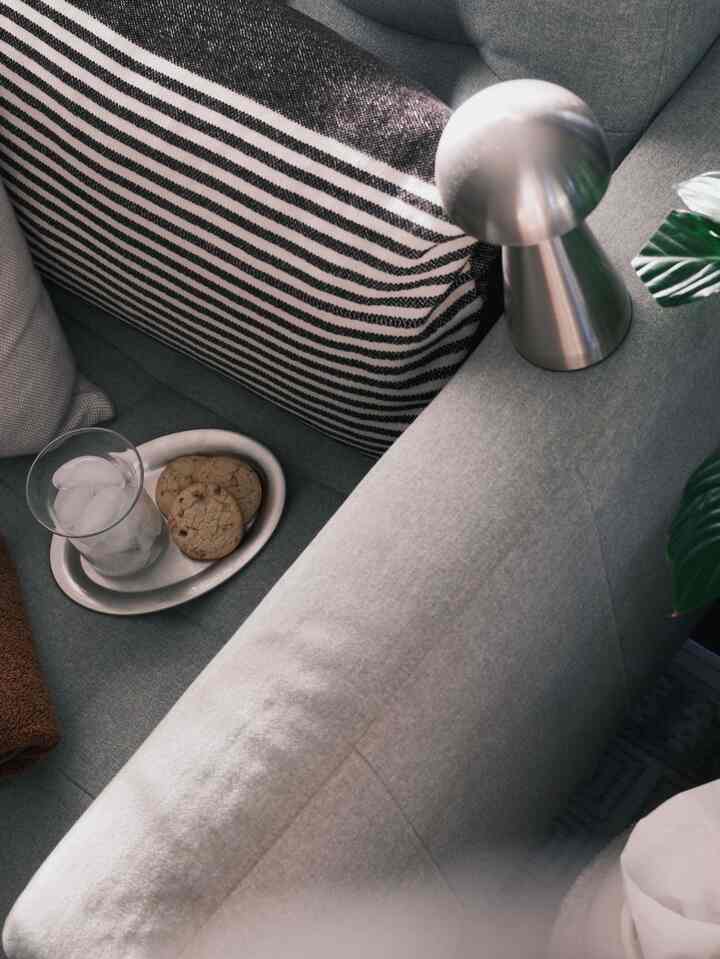 Cozy space featuring a gray-toned sofa with a silver objet, transparent glass with ice, and cookies evoking a home cafe vibe