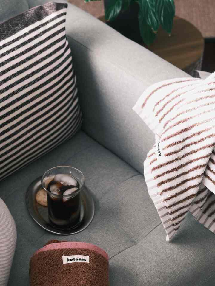 Cozy home cafe scene with gray sofa, brown and pink towels, and a glass of iced coffee