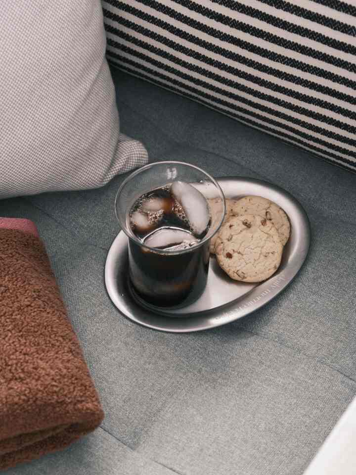 Gray-toned living room sofa setup featuring a clear glass iced Americano and stainless steel mini plate with cookies in a cozy home cafe atmosphere