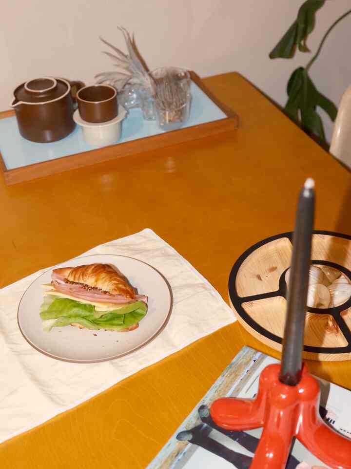 Warm natural-toned dining room featuring a croissant sandwich on a plate and traditional tea set on a wooden table, creating a cozy atmosphere