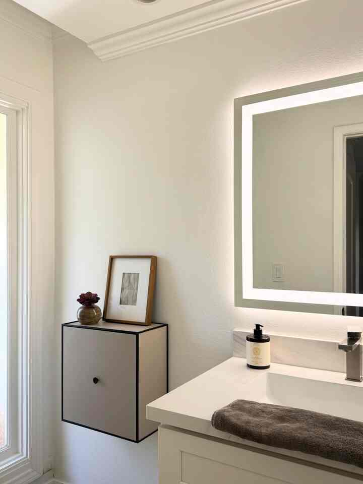 White and beige toned bathroom featuring a vanity mirror and wall storage cabinet in a simple, modern setting