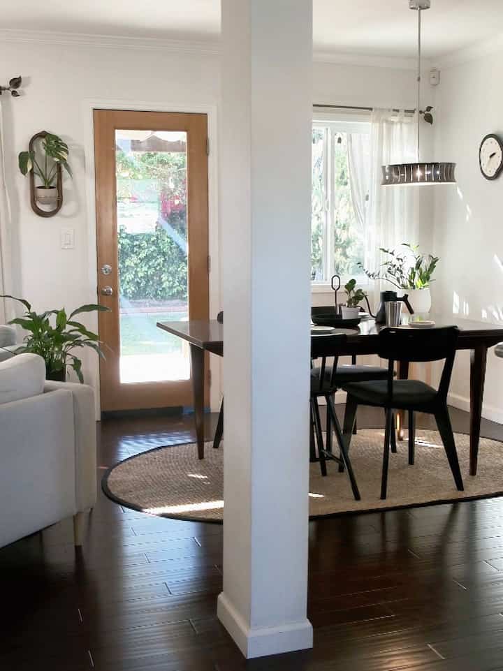 Bright white walls and natural wood-tone dining table with black chairs in a modern cozy dining and living space