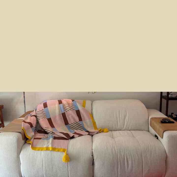 A cozy living room space featuring a natural beige sofa with a colorful throw blanket draped over it