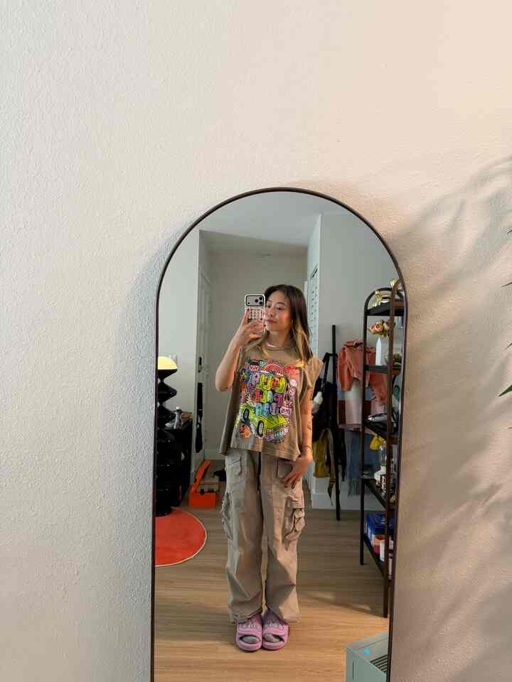 Compact room with white walls and wood flooring featuring an arched mirror and a clothes rack