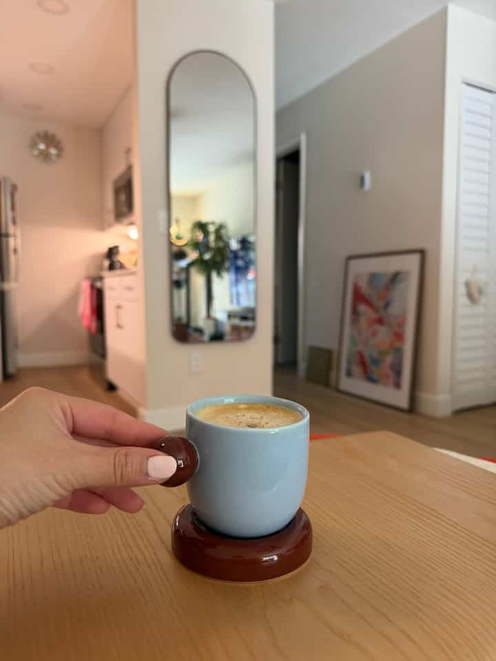 Natural-tone kitchen and partial living space with coffee cup on table in foreground, creating a cozy home cafe atmosphere