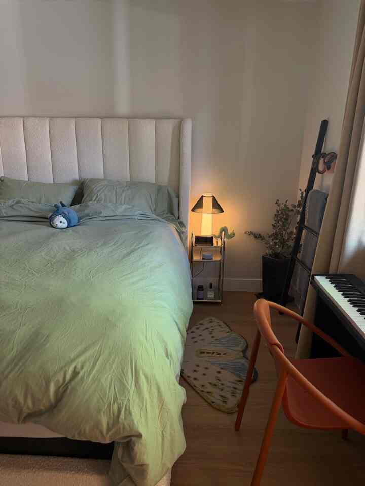 Natural color tone bedroom featuring a large bed, side table, orange chair, and digital keyboard creating a cozy atmosphere