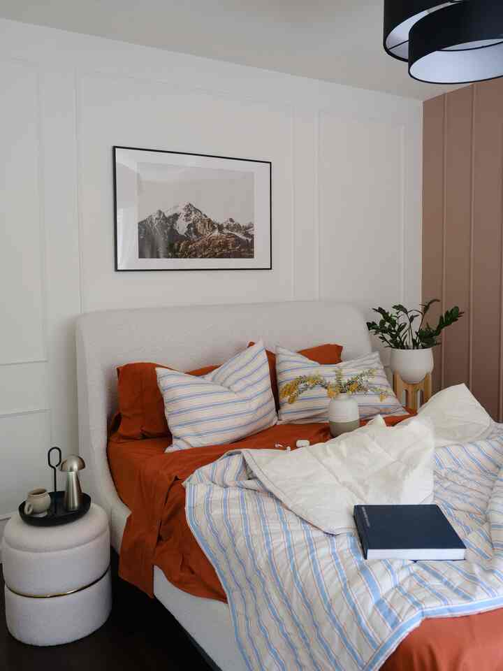 White and orange toned bedroom featuring white upholstered bed and striped bedding in a minimal and natural space