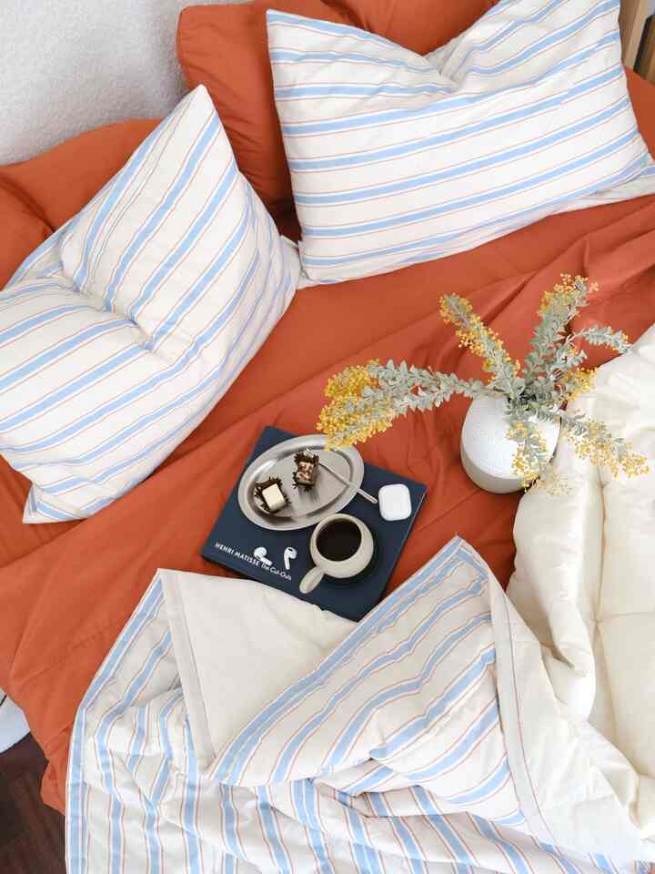 Bedroom dominated by warm orange tones with blue striped bedding, a mug of coffee, and yellow floral decor creating a cozy atmosphere
