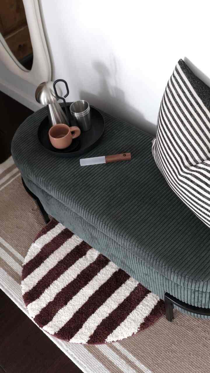 Dark green bench topped with decorative objets, striped cushion, and brown-white rugs in a modern entrance area