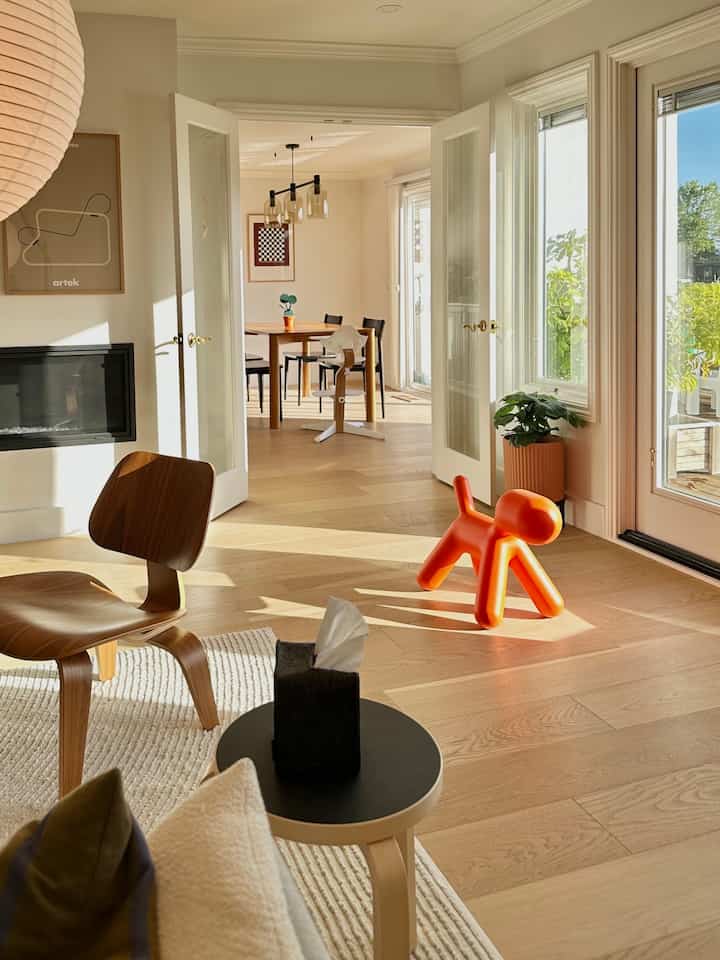 Bright white and wood-tone living and dining rooms feature a distinctive Magis dog chair and a baby high chair, creating a warm atmosphere