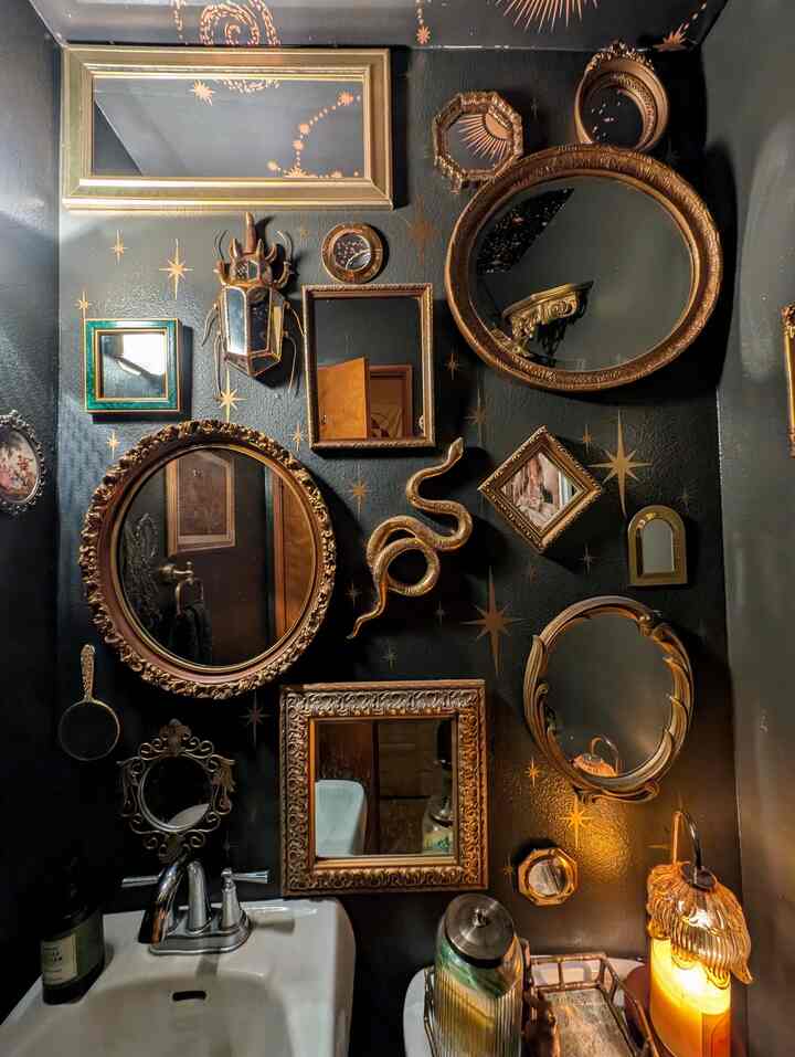 Black-walled gothic style powder room featuring gold decorative mirrors and unique art pieces with warm ambient lighting